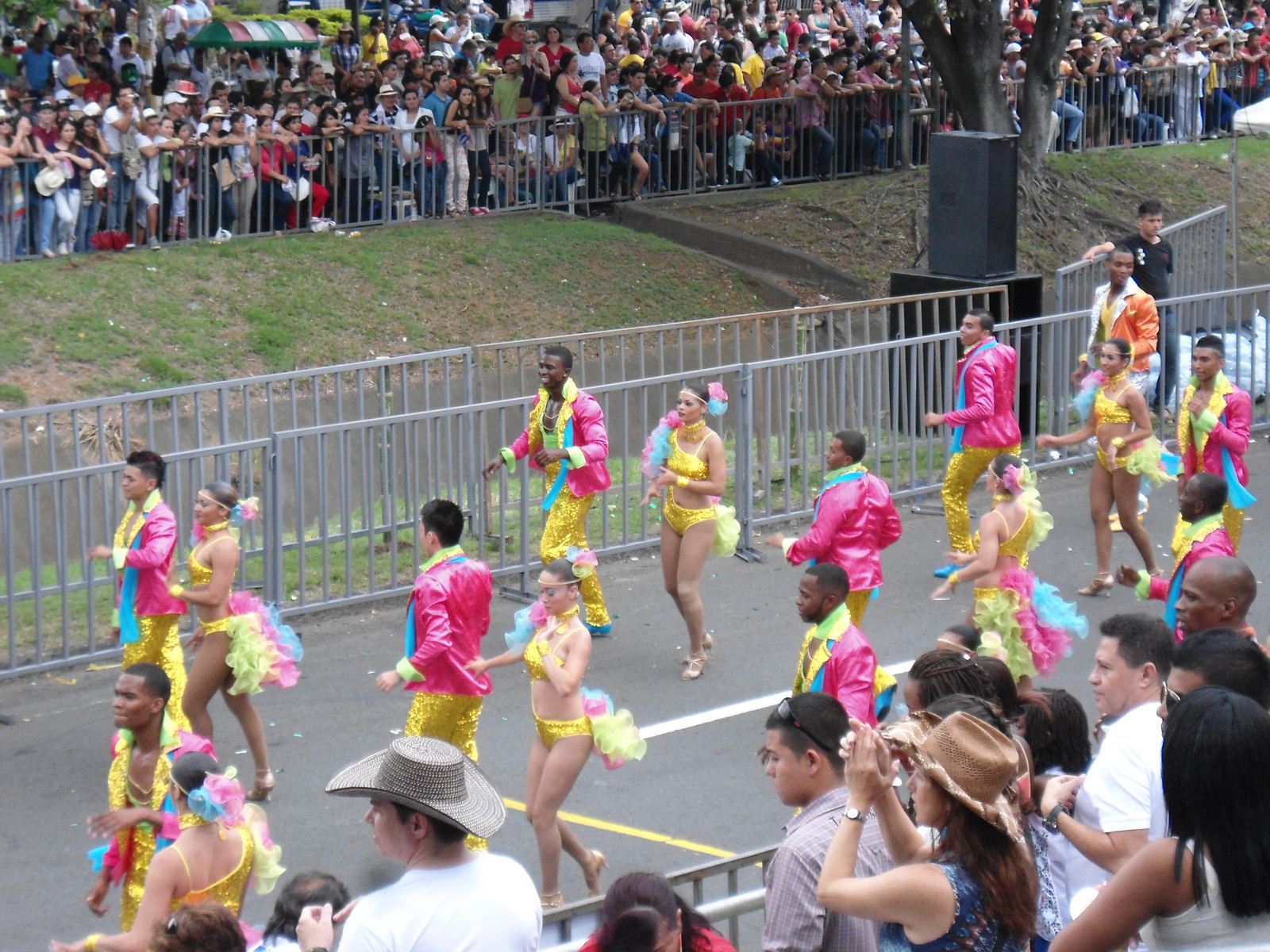 Salsa dancers in bright pink and yellow costumes parade down a street during the Feria de Cali