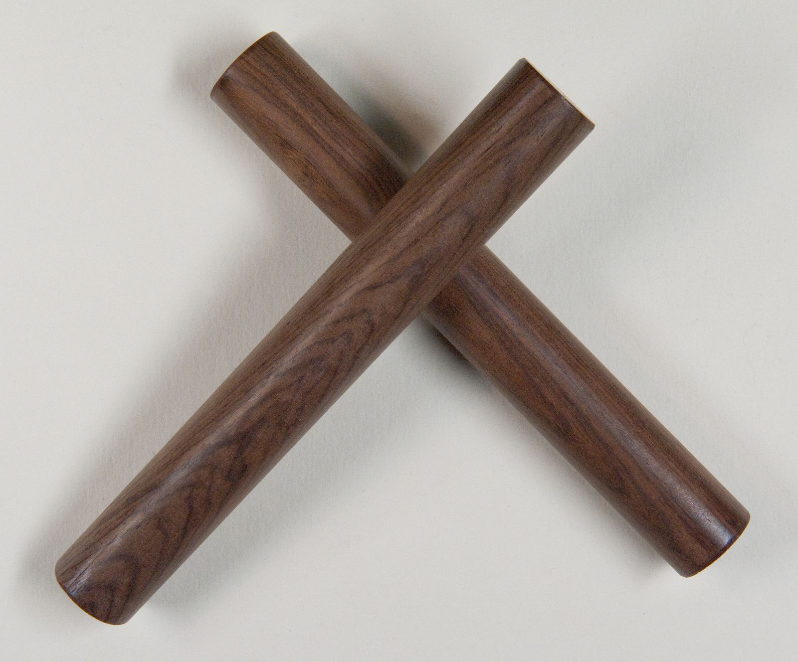 A pair of dark wooden claves crossed on a white background