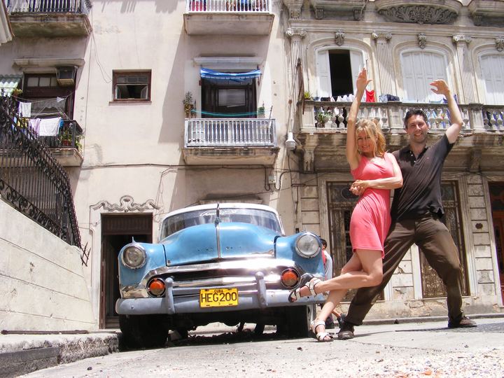 A couple dancing casino on a Havana street beside a blue vintage car
