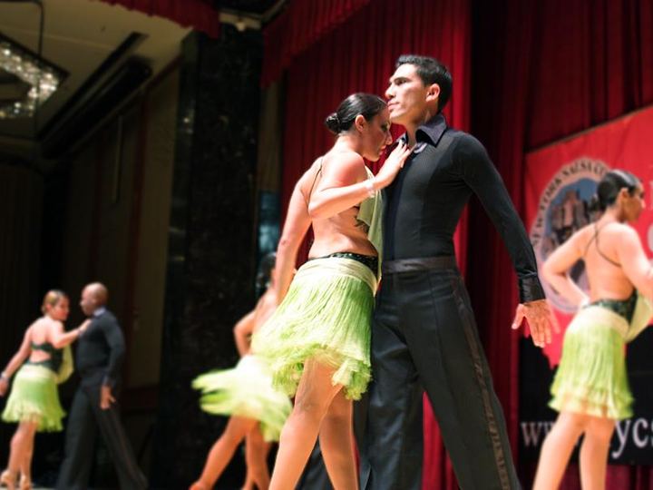 Salsa dancers in matching green outfits perform on a stage in New York